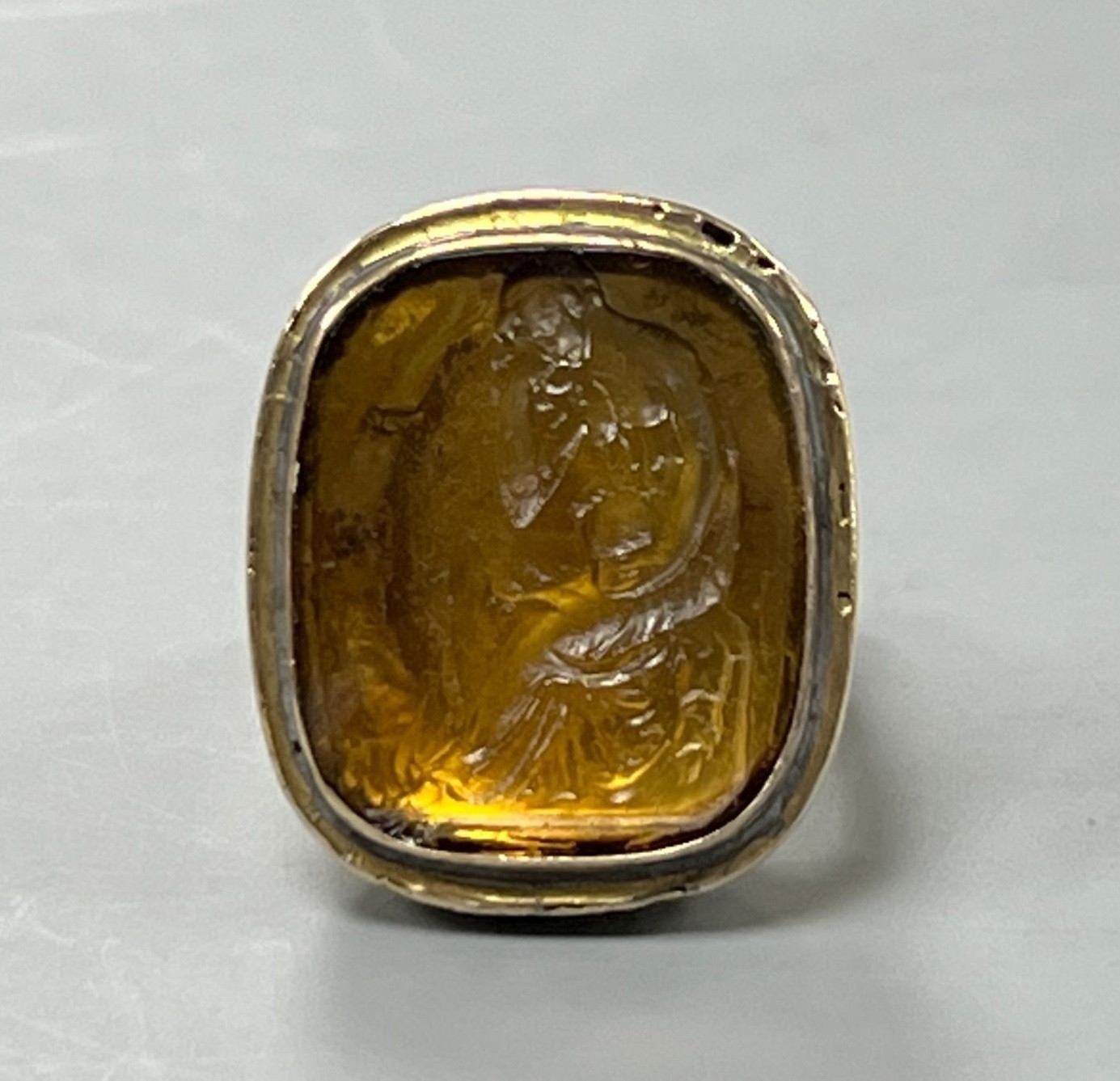 A 19th century yellow metal and intaglio yellow paste set ring, carved with 'The Thinker' after Rodin, size I, gross 8.7 grams.